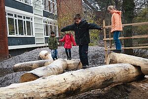 Hügelstrukturen_Lernräume_außen Kinder balancieren auf Holzstämmen im Freien