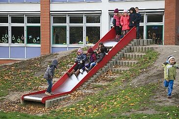 Hängerutsche_Lernräume_außen Kinder rutschen eine Rutsche im Freien hinunter